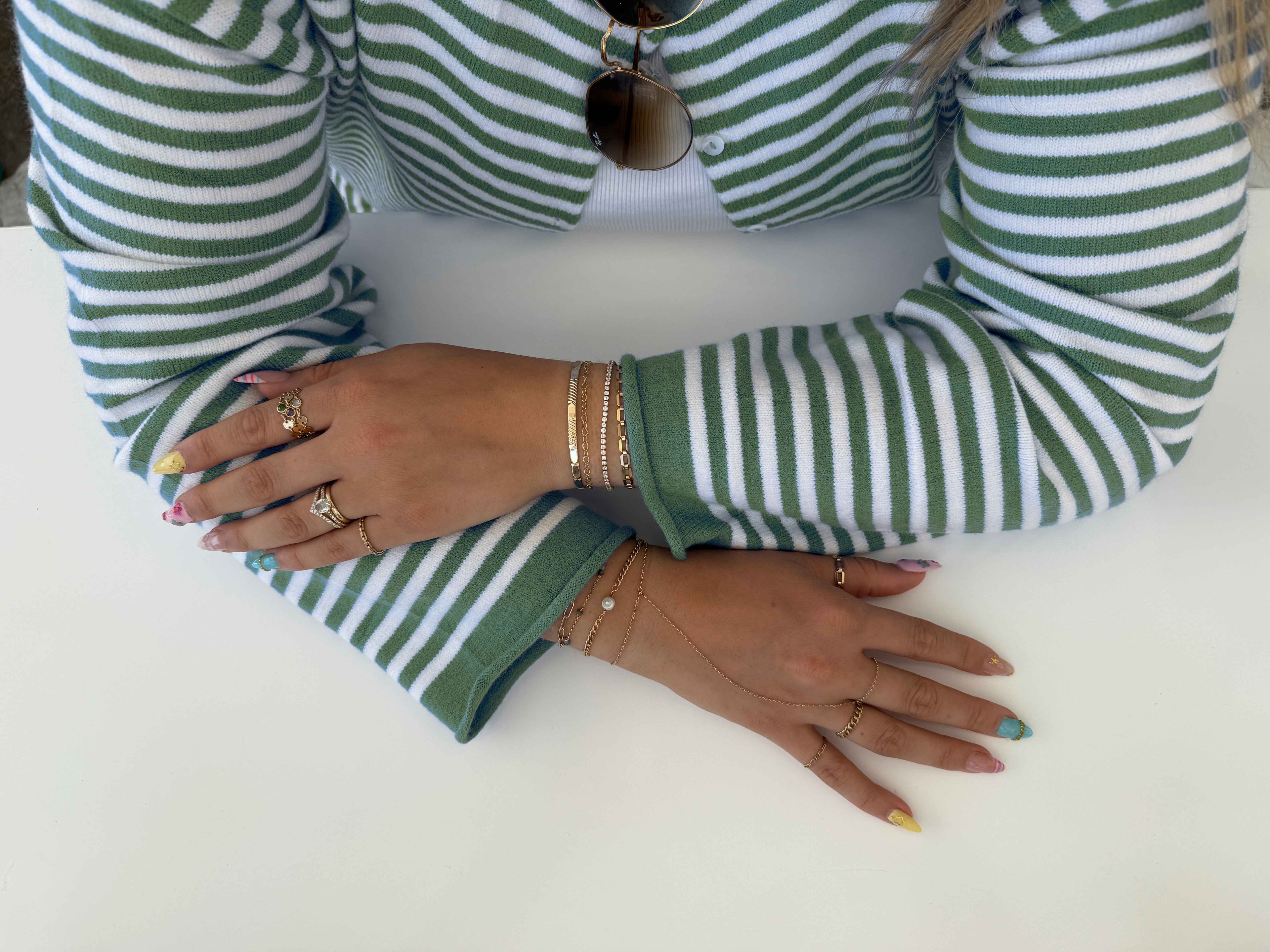Layered gold permanent jewelry bracelets and rings stacked on two wrists, Pearl & Palm Southwest Florida