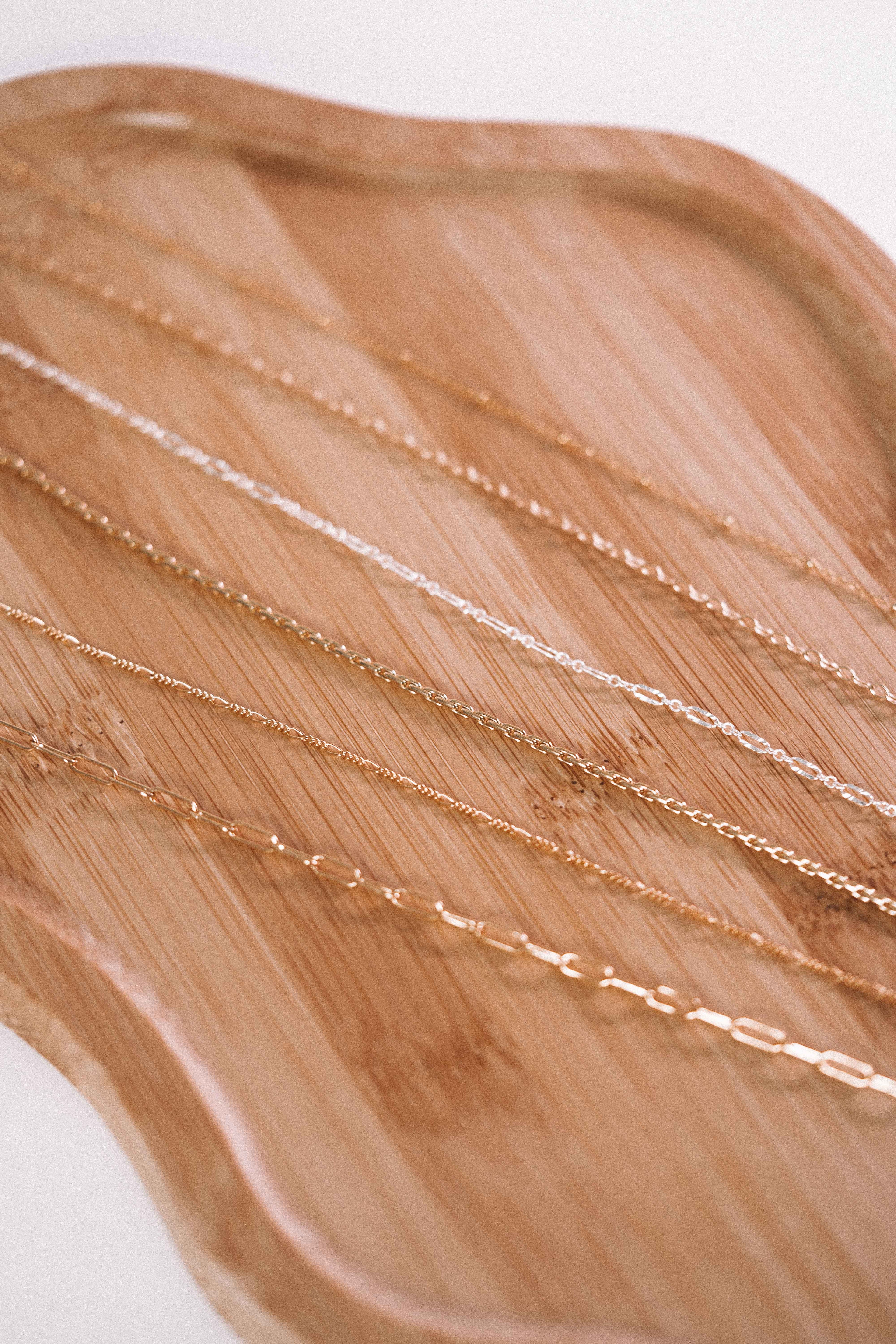 Gold permanent jewelry bracelets and chains displayed on a wooden surface
